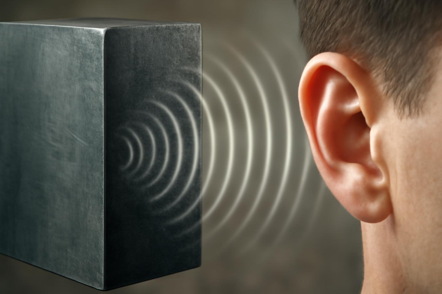 Egy fém blokk mellett álló ember fülét mutatja, ahonnan a hanghullámok terjednek.